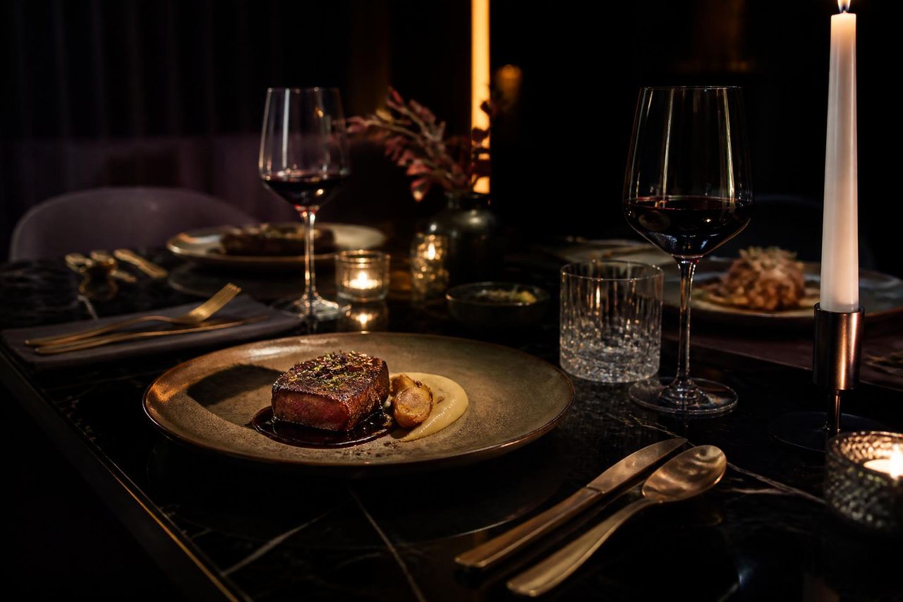 Candlelit black marble dining table set with plated courses, glassware and fine cutlery